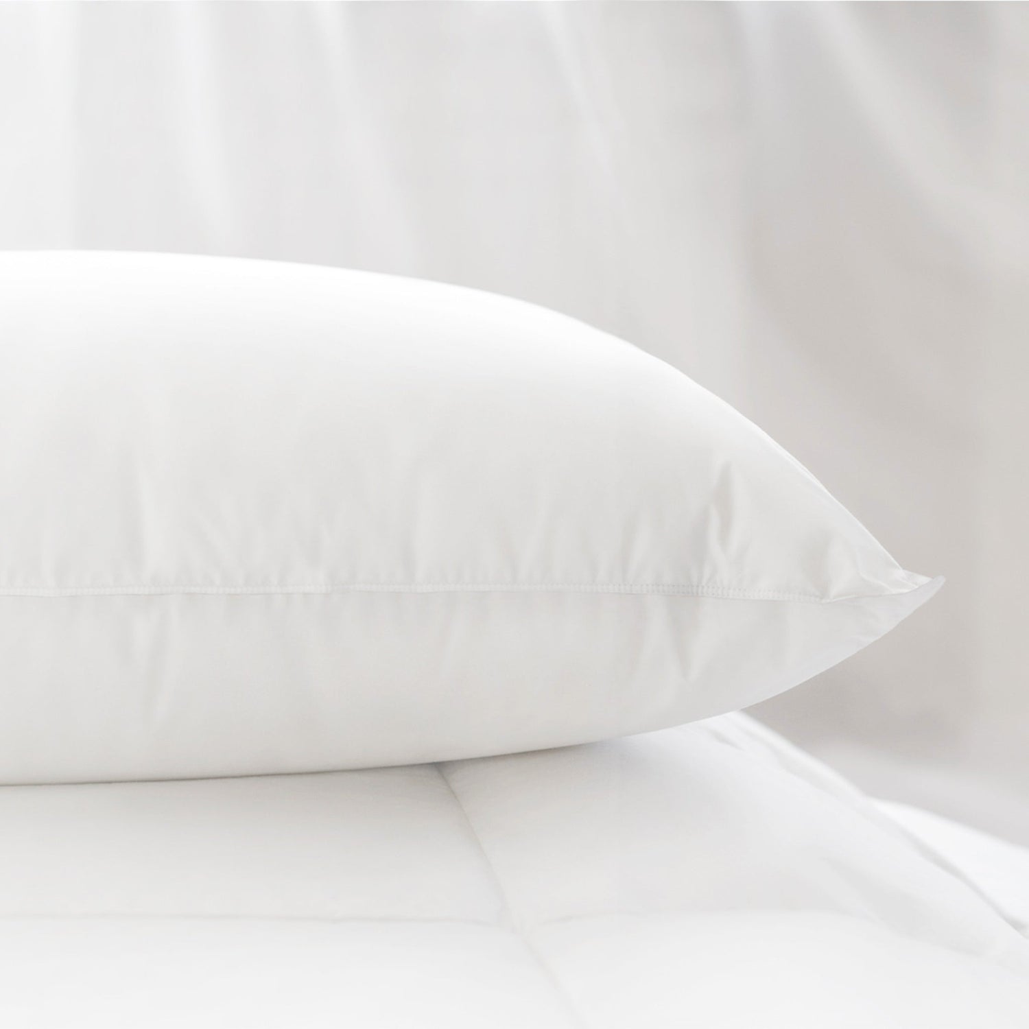 Luxurious Aurora Lilot Down Pillow atop a duvet, with tulle swaying in the wind in the background. 