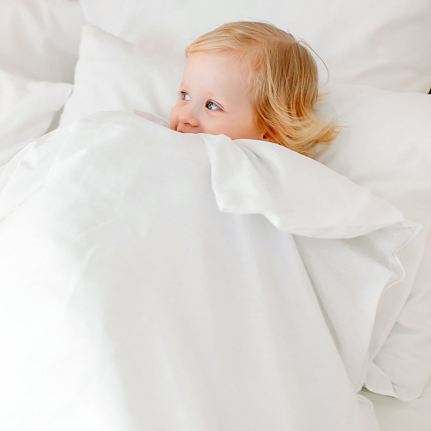 A charming baby hiding under a white blanket. Aurora Lilot Junior collection.