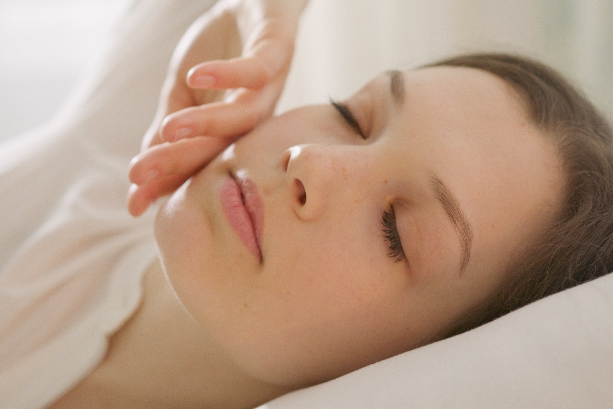 A woman peacefully resting in bed with her eyes closed, head on a Aurora Lilot down pillow, moments before waking up.