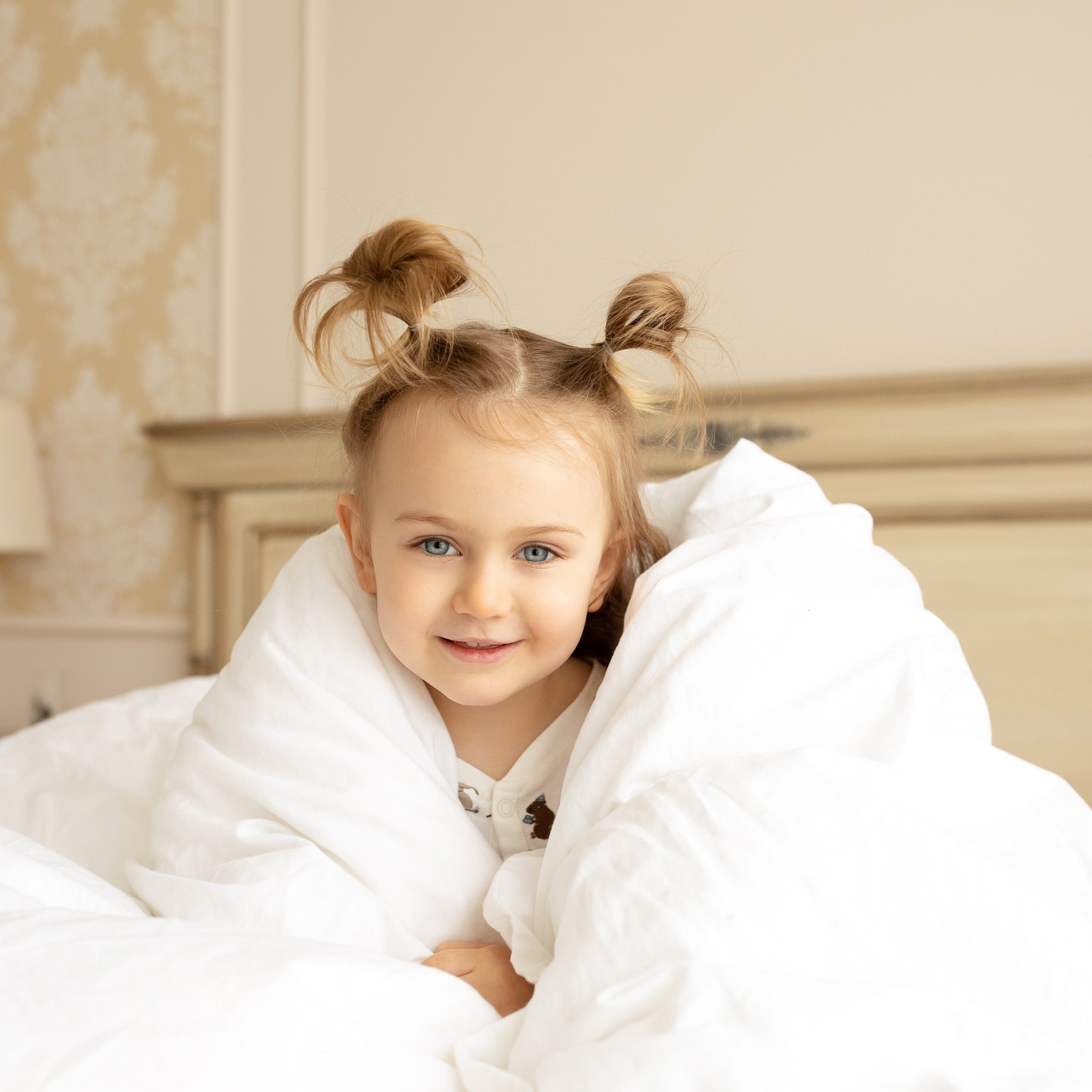 Red-haired little girl sitting on a bed, wrapped in an extra-warm winter duvet by Aurora Lilot, surrounded by cozy and warm bedding.